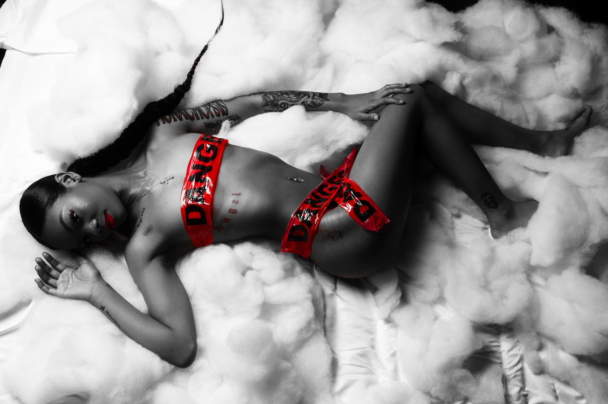 Artistic black-and-white boudoir portrait of a woman reclining on soft bedding, wearing red lingerie that contrasts against the monochrome scene, captured in a tasteful, fine-art style emphasizing form, confidence, and self-expression.