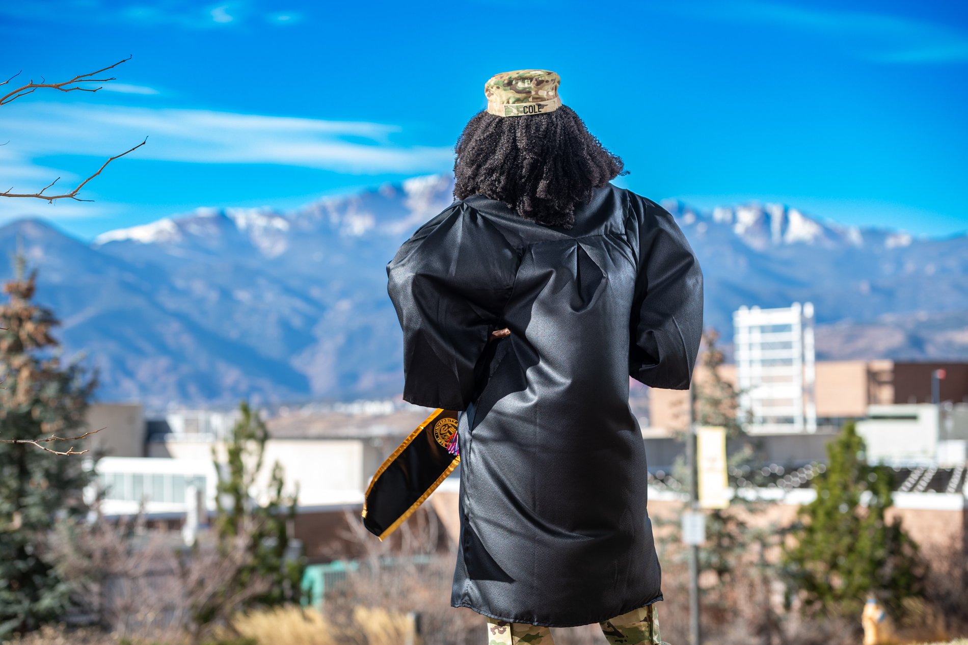 A soldier-graduate faces Pikes Peak in cap and gown