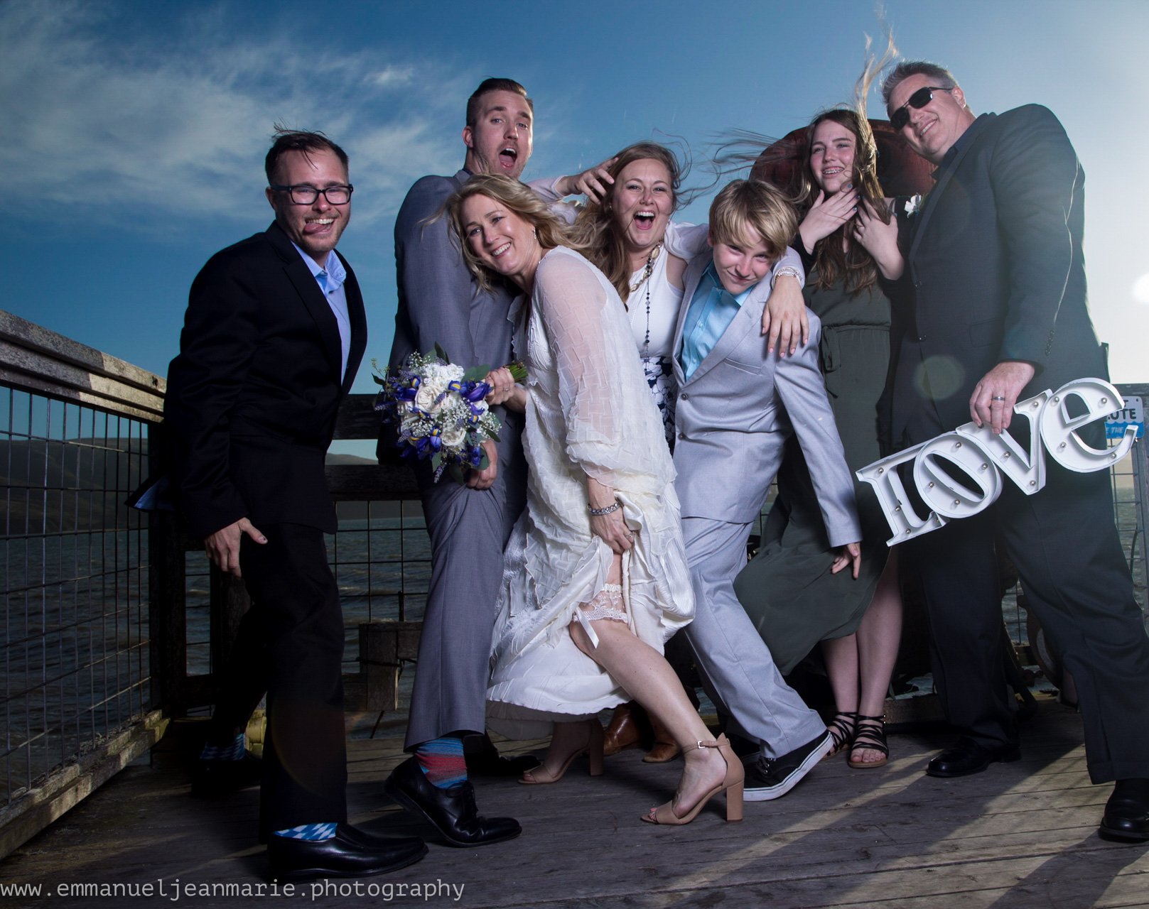 A wedding party full of joy on the pier, with a LOVE marquee, Perfectionshoots Colorado wedding photography