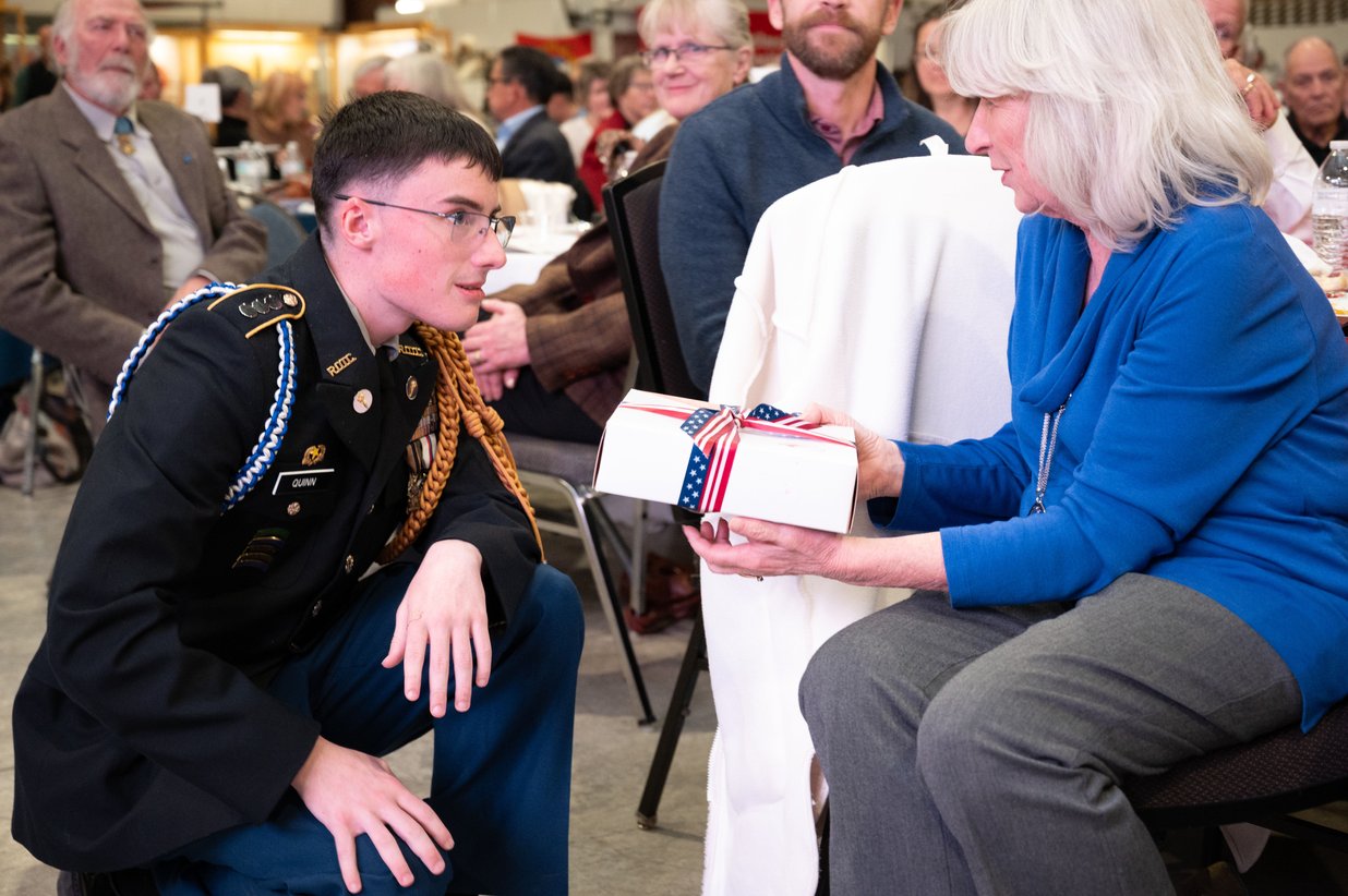 A cadet kneels to present a gift to a veteran, Perfectionshoots military and veteran event photography