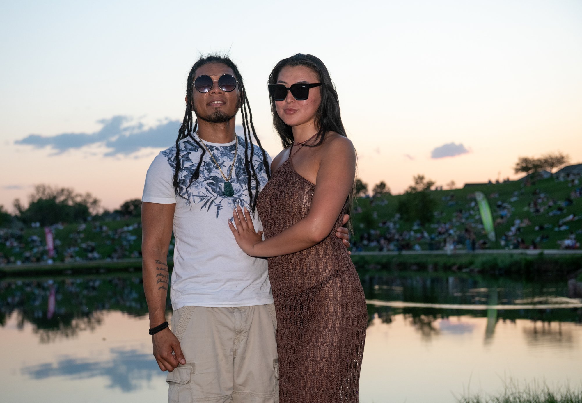 Couple poses together at golden hour by still water and lush fields, the warm sunset light capturing a moment of refined joy and the beginning of their visual legacy.