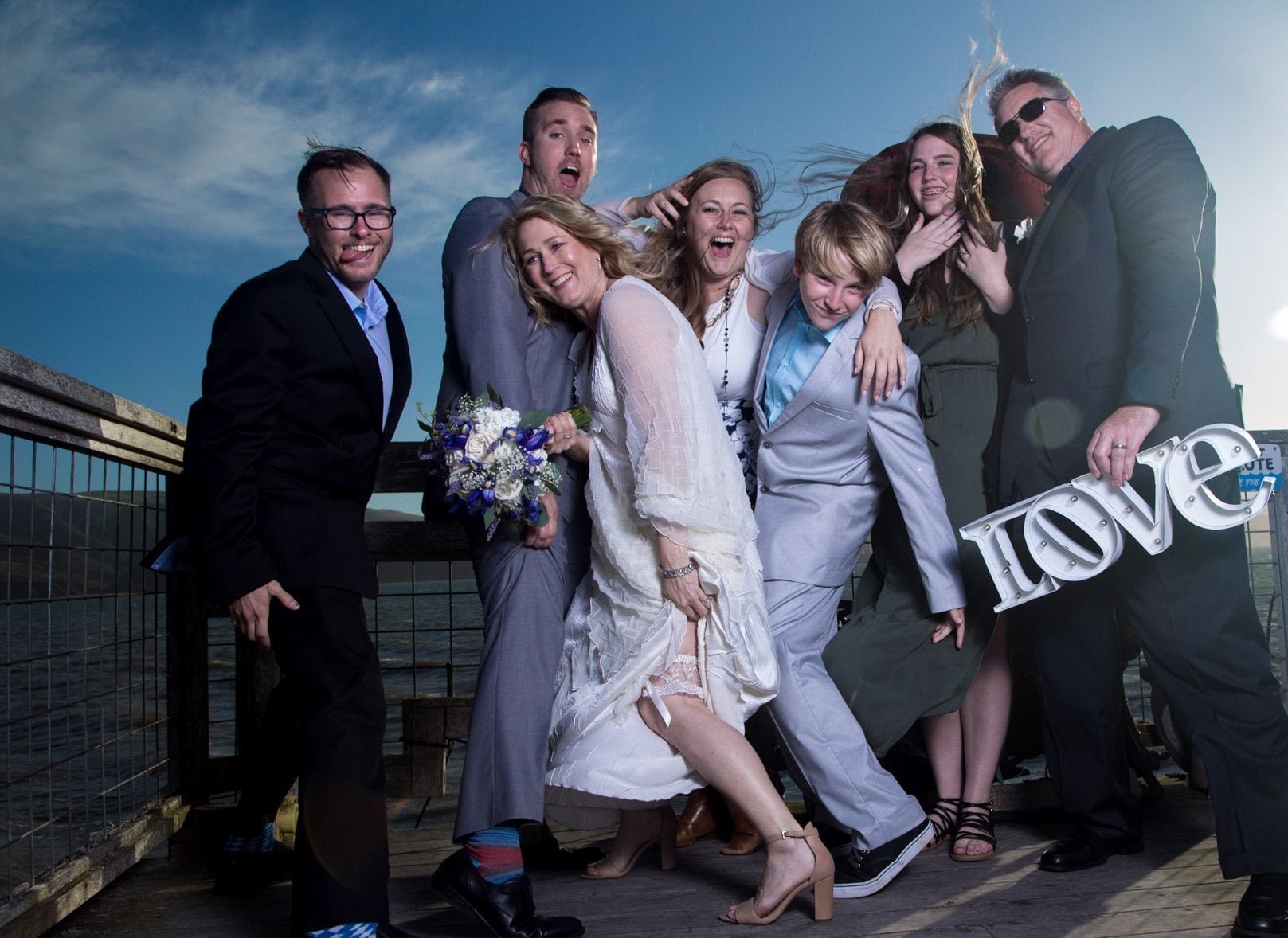 A wedding party full of joy on the pier, with a LOVE marquee, Perfectionshoots Colorado wedding photography
